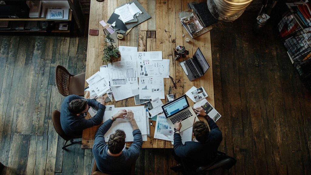 A professional team in a modern office brainstorming around a table with documents, charts, and a laptop, symbolizing collaborative PR planning.